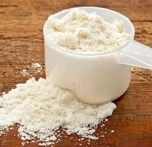 Scoop of white powder overflowing from a measuring cup on a wooden surface