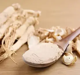 Ginseng roots and powder on a wooden spoon over a wood table