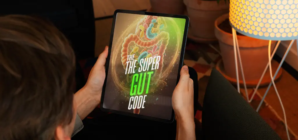 Person holding a tablet displaying "The Super Gut Code" ebook cover with a glowing digestive system illustration